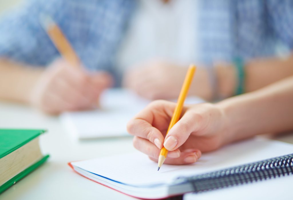 Hand of student with pencil carrying out written task or writing lecture
